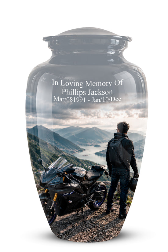 A glossy black glass cremation urn with a custom printed scenic photo of a motorcycle and a man looking at mountains, featuring white memorial text on the front, shown on a white background.