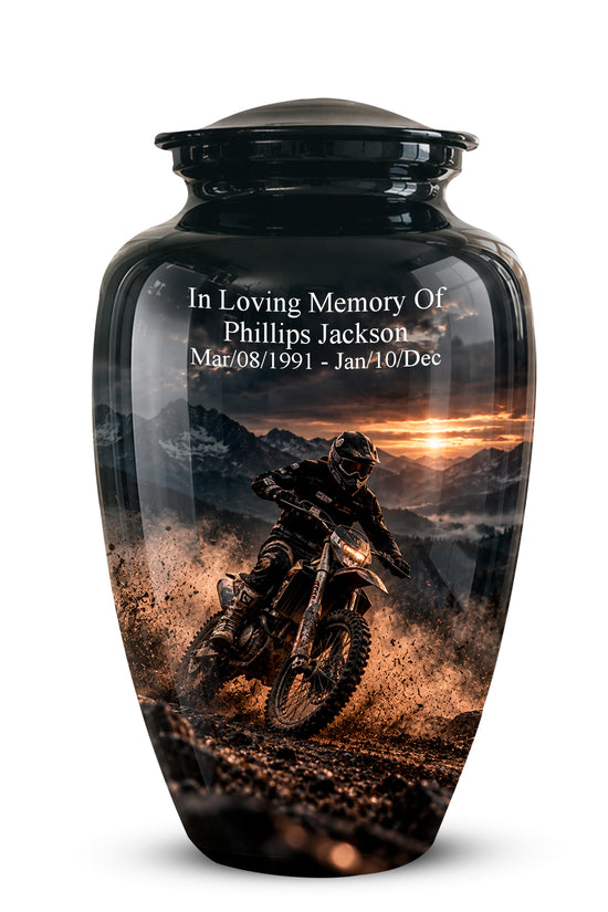 A glossy black memorial urn with a custom printed graphic of a dirt bike rider on a mountain road at sunset. White text on the upper portion reads 'In Loving Memory Of Phillips Jackson Mar,08/1991 - Jan,10/Dec'.