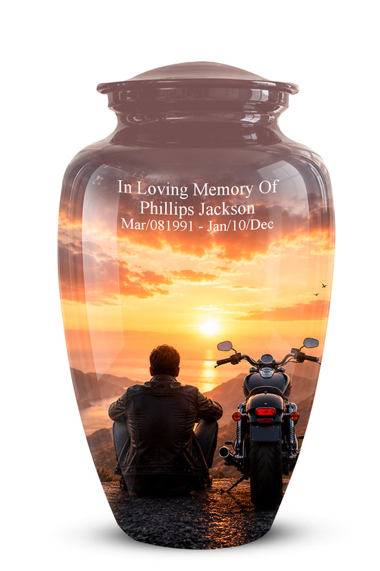 A glossy brown ceramic cremation urn with a lid, featuring a custom sunset photo print of a motorcycle and a seated figure. The text on the front reads 'In Loving Memory Of Phillips Jackson Mar/08/1991 - Jan/10/Dec'.