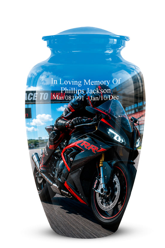 A glossy blue memorial urn featuring a printed graphic of a black and red sport motorcycle with a rider, and personalized white text reading 'In Loving Memory OF Phillips Jackson Mar/08/1991 - Jan/10/Dec'.