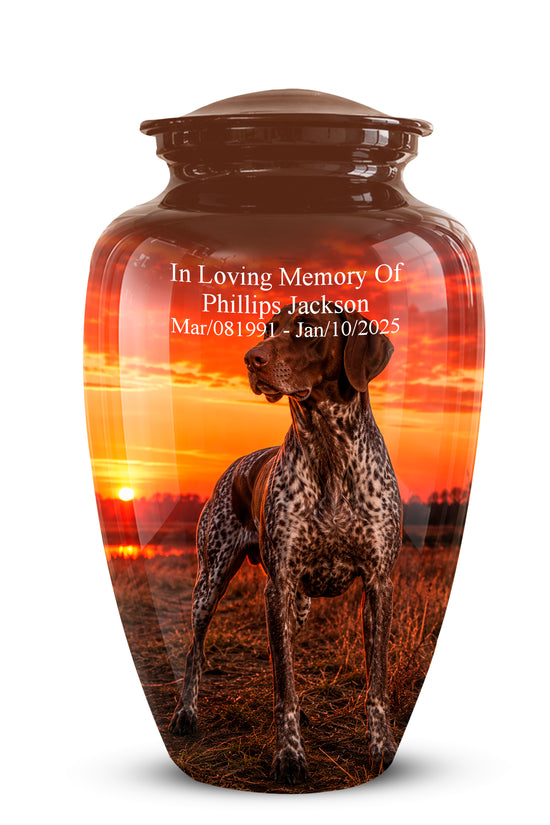 A glossy brown ceramic pet memorial urn featuring a printed sunset scene with a spotted dog standing in a field. White personalized text on the front reads, 'In Loving Memory Of Phillips Jackson Mar/081991 - Jan/10/2025.