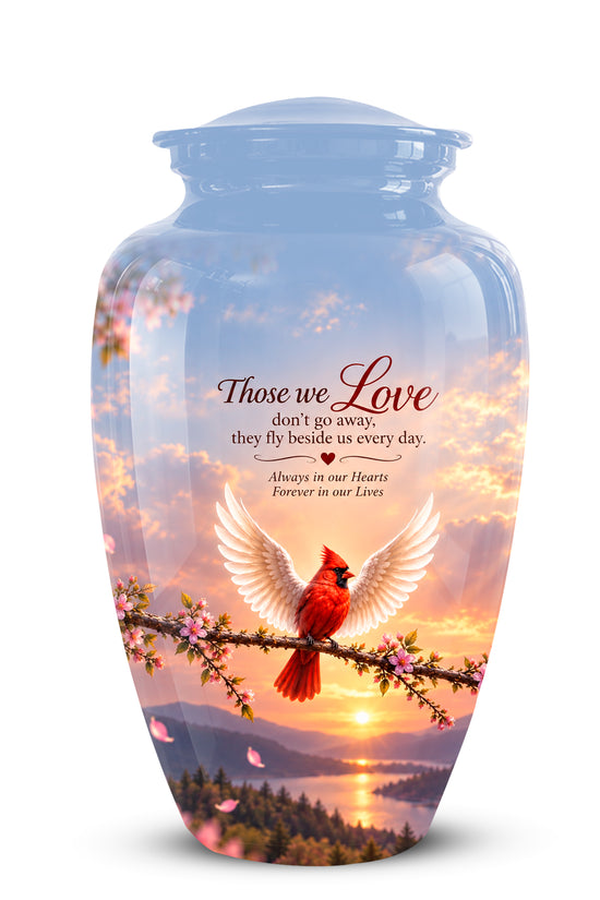 A glossy glass cremation urn with a lid, decorated with a scenic sunset landscape, a red cardinal, and white wings, with the printed text 'Those we Love don't go away, they Fly beside us every day. Always in our Hearts Forever in our Lives'.