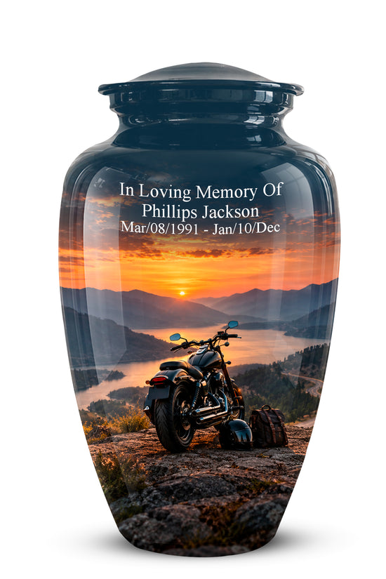 A glossy black ceramic memorial urn with a custom printed sunset landscape and a motorcycle on the front, featuring white engraved text reading 'In Loving Memory Of Phillips Jackson' and dates.