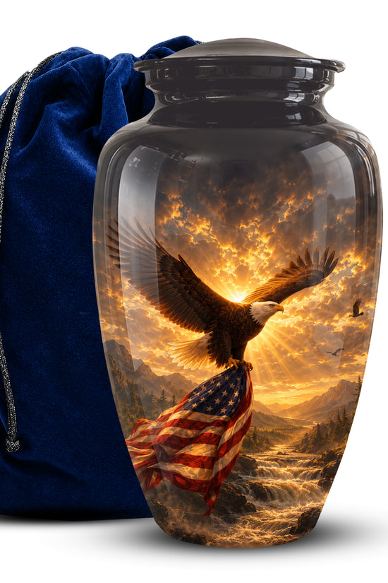 A glossy black cremation urn with a lid, featuring a printed scenic design of a bald eagle flying over an American flag at sunset, shown next to a dark blue velvet drawstring bag on a white background.