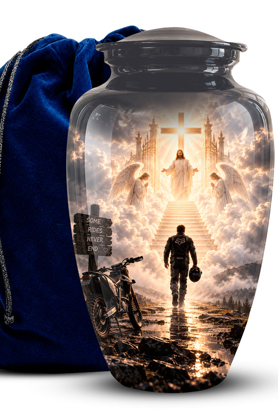 A glossy black cremation urn with a detailed religious scene printed on the front, shown next to a royal blue velvet drawstring bag on a white background.