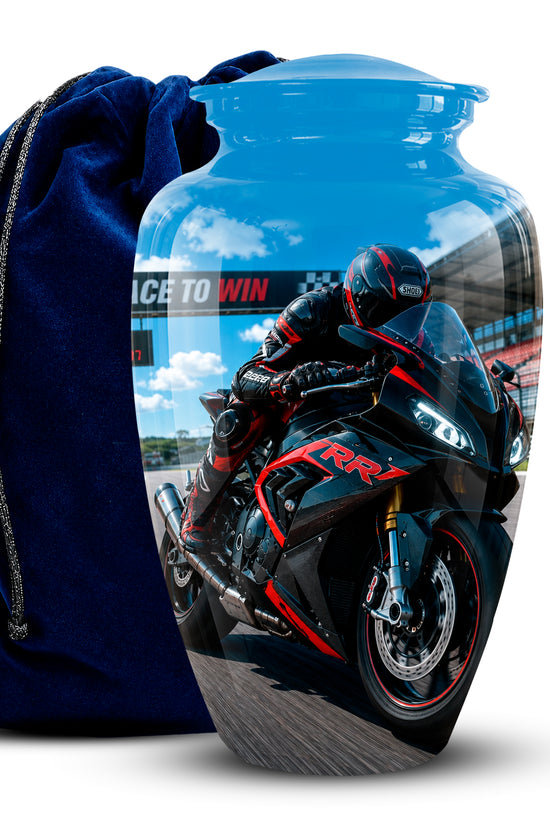 A glossy blue glass urn featuring a printed graphic of a black and red sports motorcycle racer, shown next to a dark blue velvet drawstring pouch on a white background.