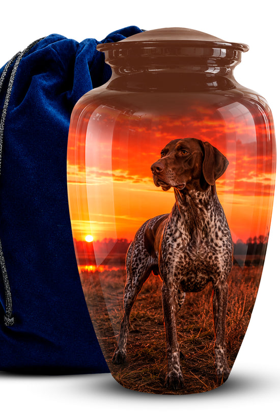 A glossy brown urn-shaped vase or keepsake jar with a lid, printed with a dog portrait over a sunset landscape. A dark blue velvet drawstring bag sits behind it on a white background.