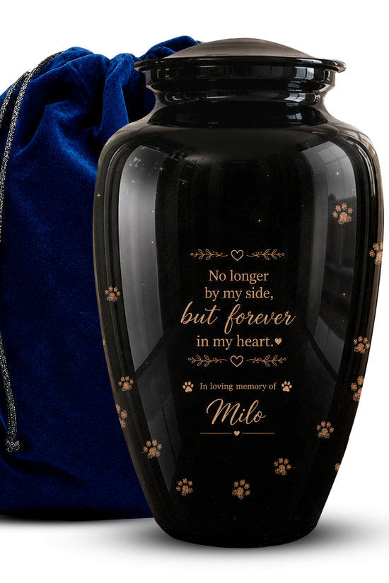 A glossy black pet memorial urn with gold engraved text and paw print details, shown next to a royal blue velvet drawstring bag on a white background.