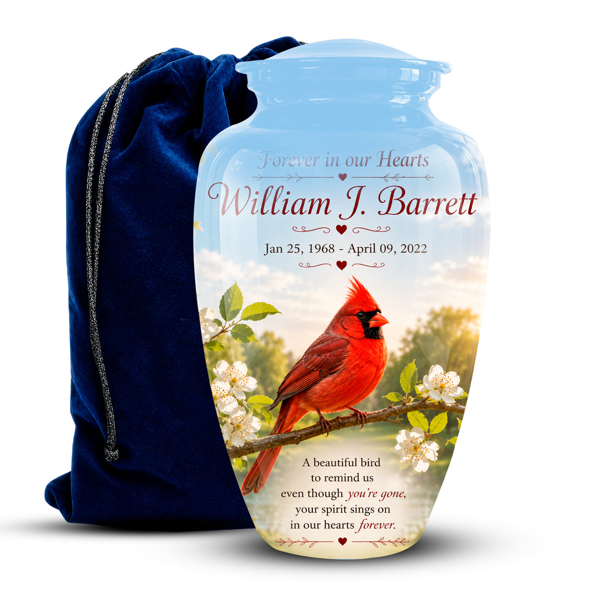 Personalized ceramic memorial urn with a blue neck and a printed photo of a red cardinal on a branch, shown next to a dark blue drawstring bag. The urn features the text 'Forever in our Hearts William J.