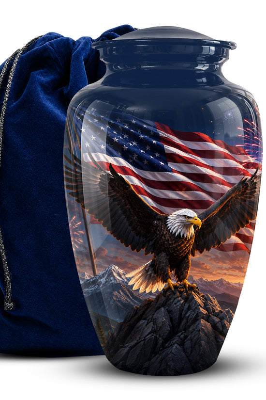A glossy glass urn with a lid, printed with a bald eagle perched on a mountain peak in front of a waving American flag, shown next to a dark blue velvet drawstring bag on a white background.