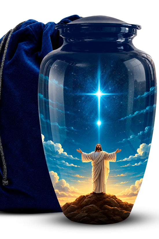 A glossy dark blue glass-style urn with a lid, printed with a religious scene of Jesus standing on a hill under a starry sky, next to a dark blue velvet drawstring bag on a white background.