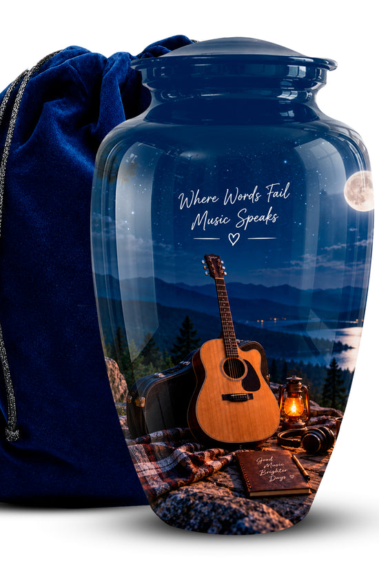 A glossy blue glass urn with a custom printed scenic design of a night mountain landscape, an acoustic guitar, and a moon, shown next to a dark blue velvet drawstring bag on a white background.