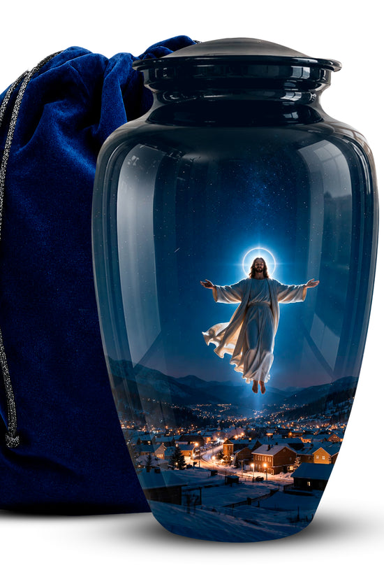 A glossy dark blue glass cremation urn with a lid, featuring a printed image of Jesus floating above a snowy village at night. A deep blue velvet drawstring bag sits behind the urn on a white background.