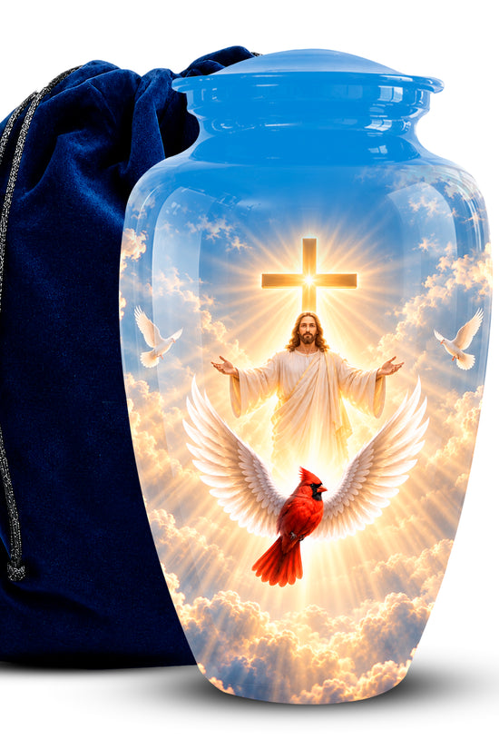 A clear glass cremation urn with a blue lid, featuring a printed religious design of Jesus with a cross, doves, clouds, and a red cardinal. A dark blue velvet drawstring bag is positioned behind the urn on a white background.