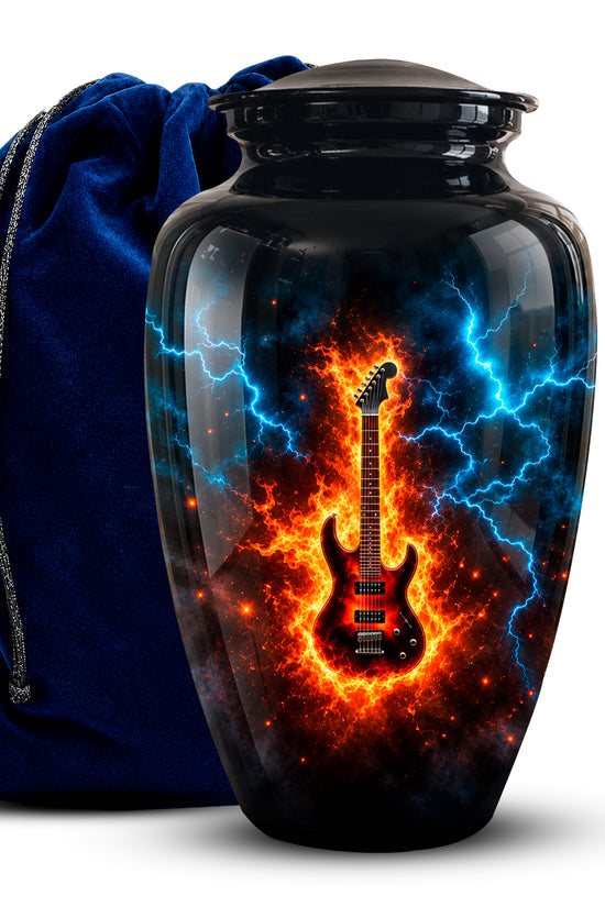 A glossy black urn-shaped vase or keepsake jar with a lid, featuring a printed design of a red electric guitar surrounded by bright orange flames and blue lightning. A dark blue velvet drawstring bag stands behind it on a white background.