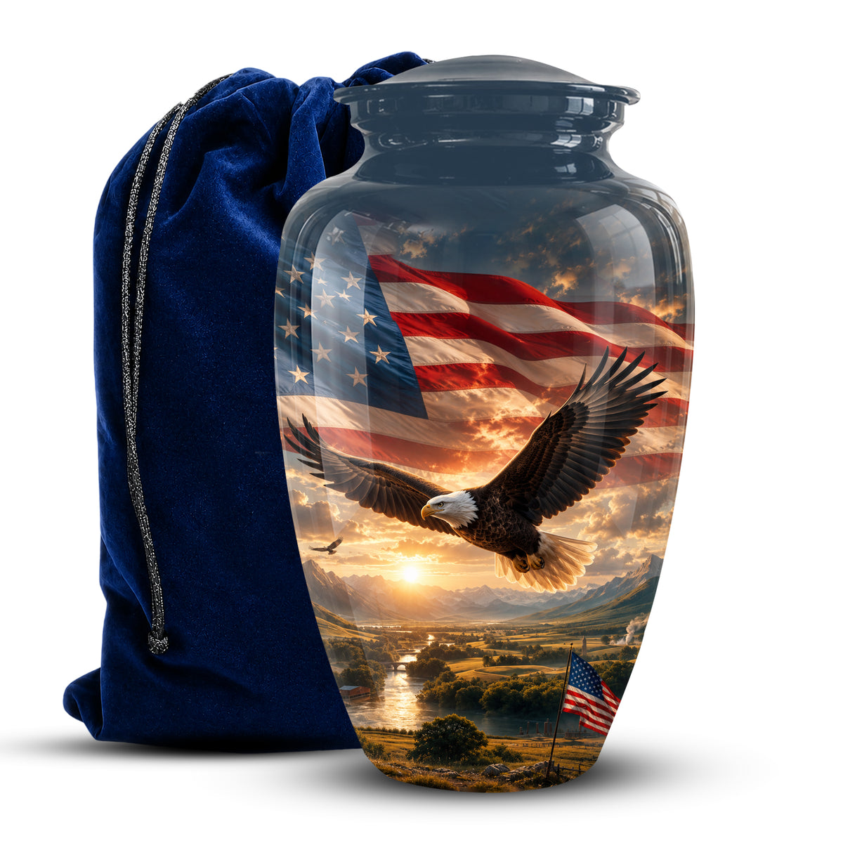 A clear glass cremation urn with a dark gray lid, featuring a printed design of a bald eagle flying over a landscape beneath an American flag. A dark blue velvet drawstring bag is positioned behind the urn on a white background.