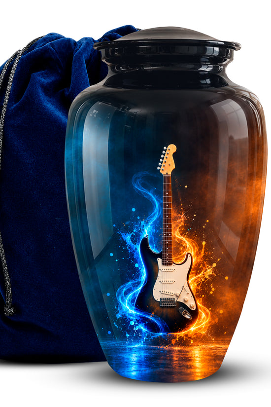 A glossy black glass urn-shaped vase with a lid, featuring a printed electric guitar design split by blue and orange flame-like swirls. A dark blue velvet drawstring bag sits behind it on a white studio background.