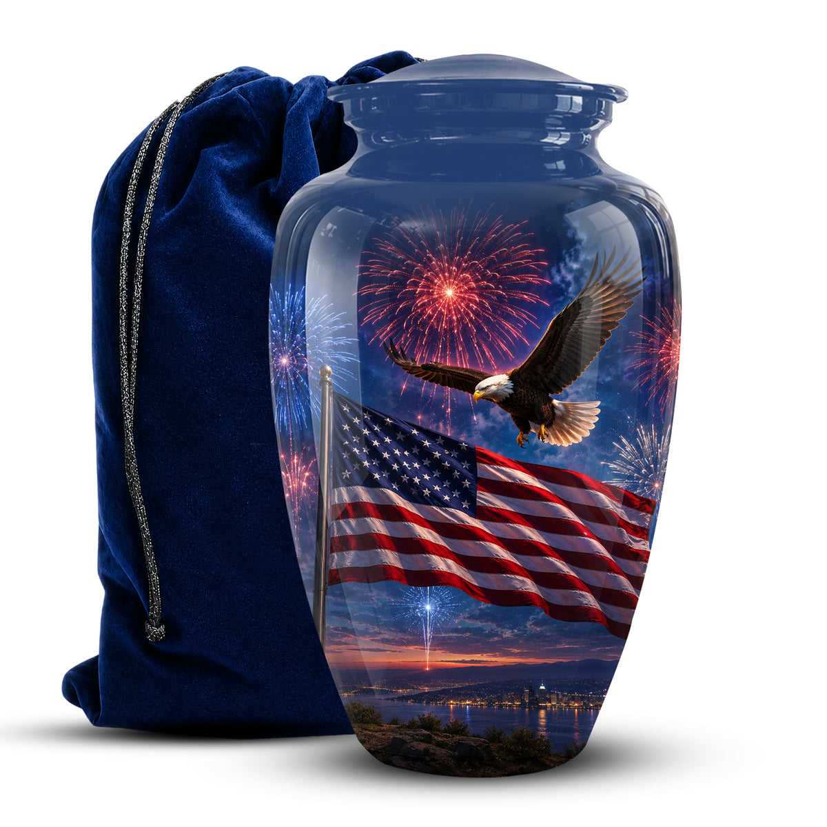 A clear glass cremation urn with a lid, printed with an American flag, bald eagle, fireworks, and sunset landscape. A dark blue velvet drawstring bag stands behind it on a white background.