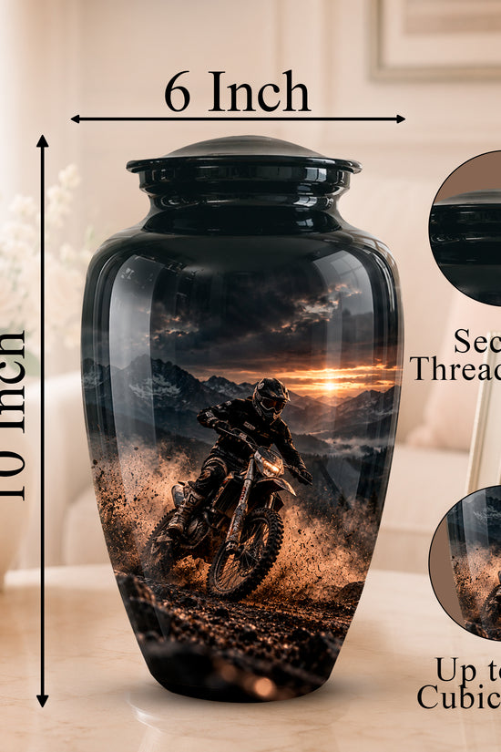 A black ceramic cremation urn with a printed motocross rider scene on the front, shown on a tabletop with dimension labels reading 10 Inch height and 6 Inch width. Circular inset images highlight the secure threaded lid and the printed design capacity up to 200 cubic inches.