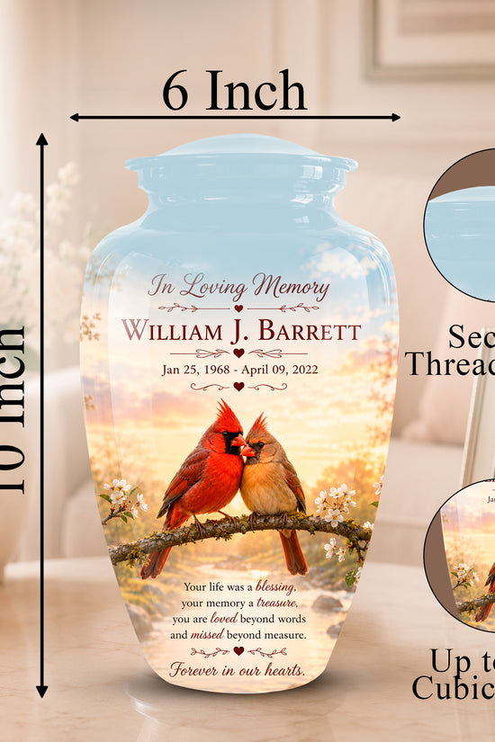 Personalized ceramic memorial vase with a threaded lid, shown on a tabletop with dimension labels indicating 6 inch width and 10 inch height. The vase features a printed design of a red cardinal on a branch against a warm sunset sky, with memorial text reading 'In Loving Memory William J.