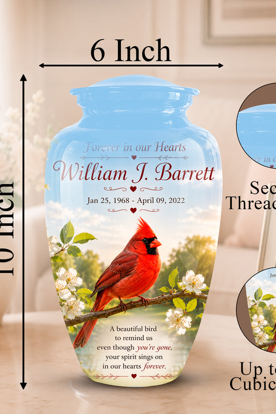 Personalized ceramic memorial urn with a blue lid and printed design of a red cardinal on a branch with white blossoms. The image includes dimension labels showing 6 inch width and 10 inch height, plus circular insets showing the secure threaded lid and the printed design detail, all on a softly lit indoor background.