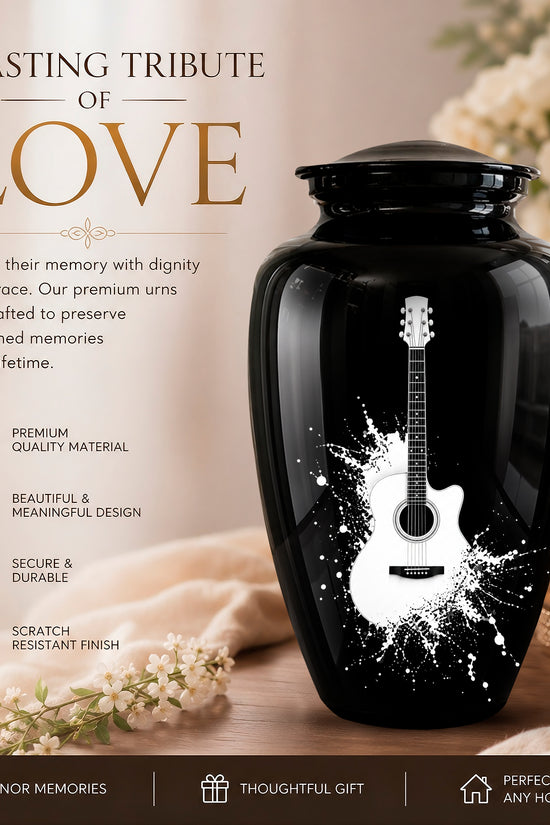 A glossy black ceramic or glass memorial urn with a white guitar graphic and white paint splatter design, displayed on a wooden surface with flowers, a candle, and promotional text reading 'A LASTING TRIBUTE OF LOVE'.