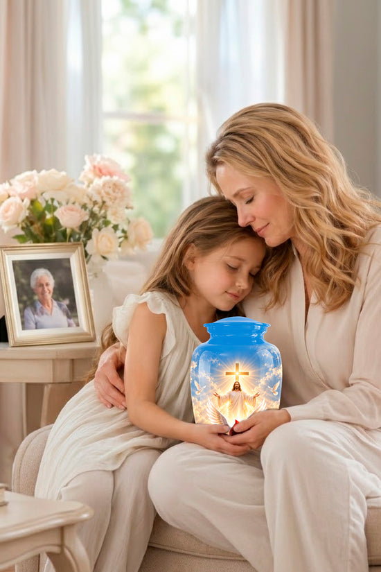 A woman and a young girl sit together on a beige sofa in a bright living room, holding a glowing blue glass jar with a printed image of Jesus. A framed photo and vase of flowers sit on a side table nearby.
