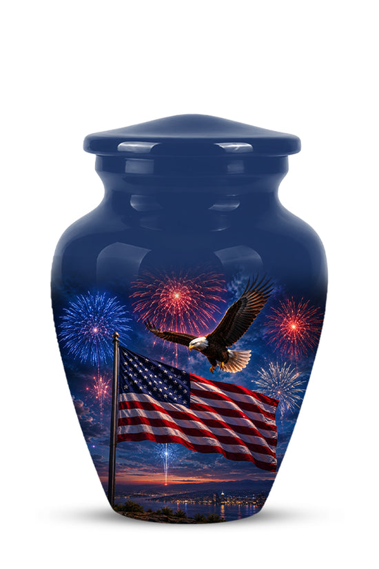 A glossy dark blue urn with a lid, featuring a printed design of an American flag waving, an eagle in flight, and fireworks over water at sunset.