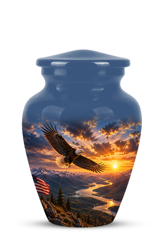 A glossy blue ceramic cremation urn with a lid, featuring a printed scenic design of a bald eagle flying over a mountain river valley at sunset with an American flag in the foreground.