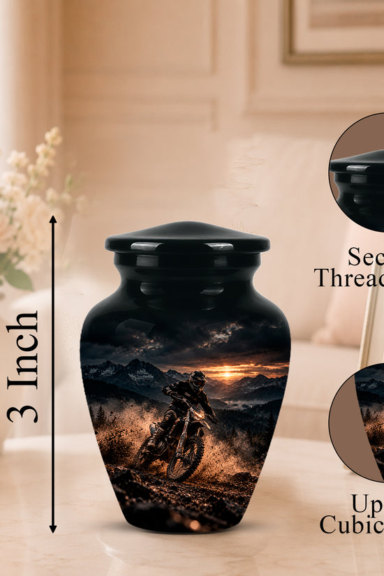Black cremation urn with a printed motorcycle racing sunset design, shown on a tabletop with a flower vase and framed photo in a softly lit room. Callout text indicates 3 inch height and circular insets showing the secure threaded lid and up to 3 cubic inch capacity.