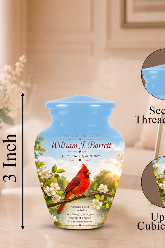 Personalized ceramic urn with a blue lid and a printed design of a red cardinal on white blossoms, shown on a tabletop with dimension callouts and circular inset details about the secure threaded lid and cubic capacity.