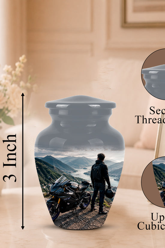 A memorial urn vase with a printed scenic photo of a motorcyclist on a mountain road, shown on a tabletop in a softly lit room. The image includes a 3-inch height marker, a close-up inset labeled 'Secure Threaded Lid,' and a circular inset labeled 'Up to 3 Cubic Inches.