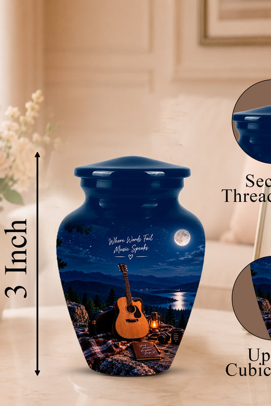 A glossy dark blue urn-shaped memorial vase with a lid, shown on a tabletop in a softly lit room. The vase features a printed night scene with a guitar, candles, moon, and memorial inscription.