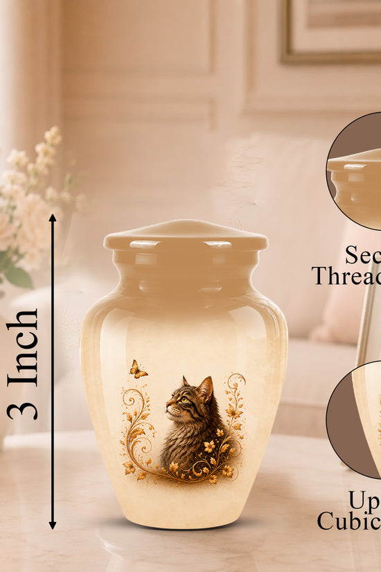 A cream-colored cremation urn with a printed cat illustration and gold scroll details, shown on a tabletop in a softly lit room. The image includes a height marker reading 3 Inch and two circular inset callouts highlighting the secure threaded lid and up to 3 cubic inch capacity.