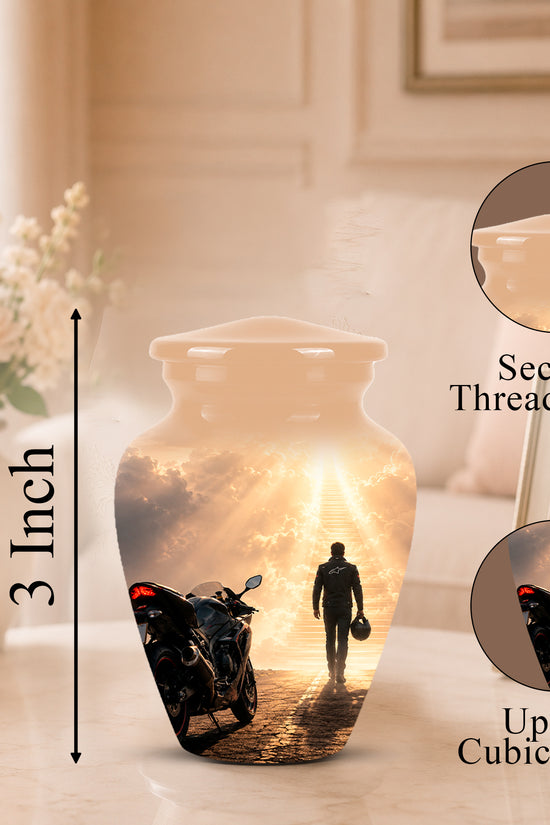 A ceramic cremation urn with a printed sunset scene featuring a motorcycle and a walking silhouette, shown on a tabletop with a vase of flowers and framed photo in the background. The image includes dimension callouts indicating 3 inch height and 3 cubic inch capacity, plus close-up inset circles labeled 'Secure Threaded Lid' and 'Up to 3 Cubic Inches'.