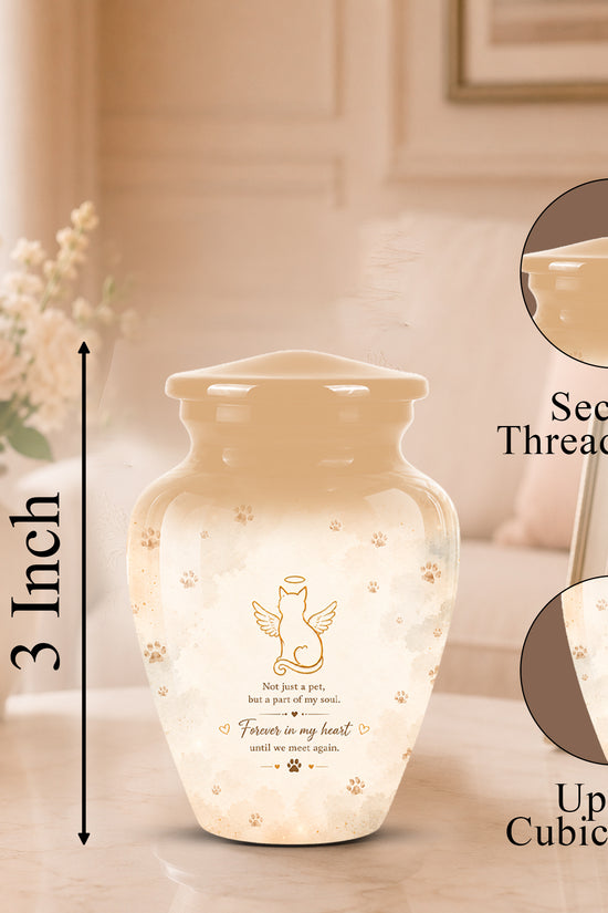 A cremation urn shown in a softly lit indoor setting with measurement callouts and detail insets. The urn is a small beige jar with a threaded lid, decorated with a gold angel graphic and paw prints on a white body.