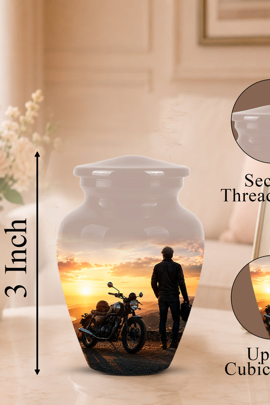 Personalized ceramic urn with a printed motorcycle and sunset photo design, shown on a tabletop with a blurred home interior background. The image includes a 3-inch height marker, a close-up inset of the secure threaded lid, and a circular inset showing up to 3 cubic inches of space for a photo.