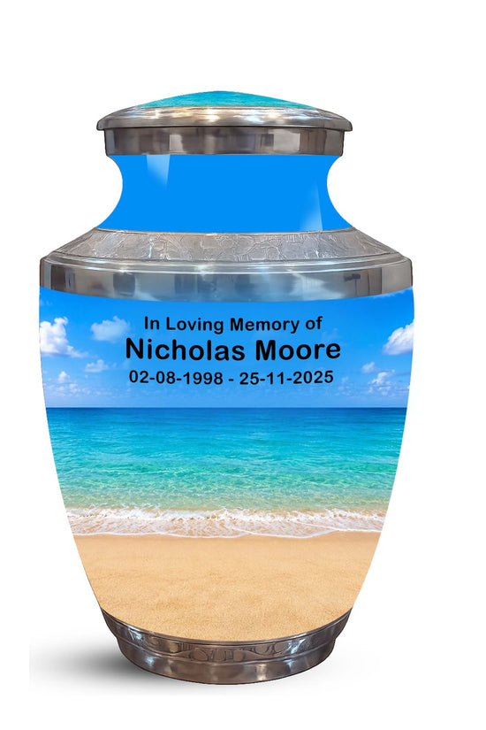 A memorial urn with a tropical beach print, featuring a blue sky and ocean design with custom text reading 'In Loving Memory of Nicholas Moore' and dates, set against a plain white background.