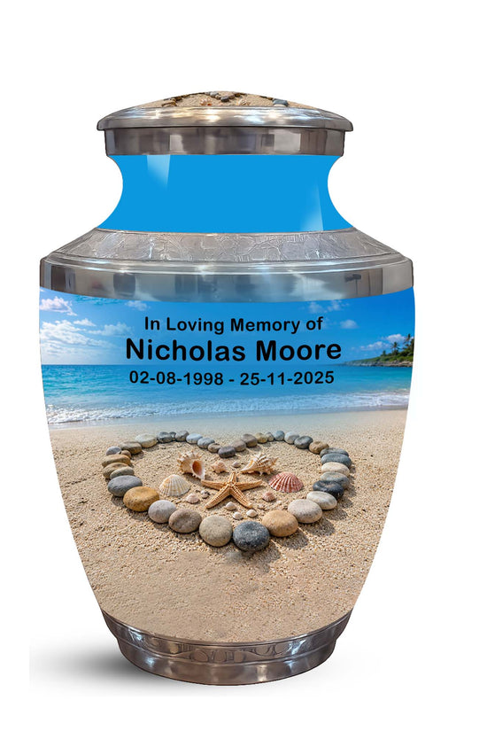 A memorial urn with a lid, featuring a custom printed beach scene on the front. The text on the urn reads 'In Loving Memory of Nicholas Moore 02-08-1998 - 25-11-2025'.