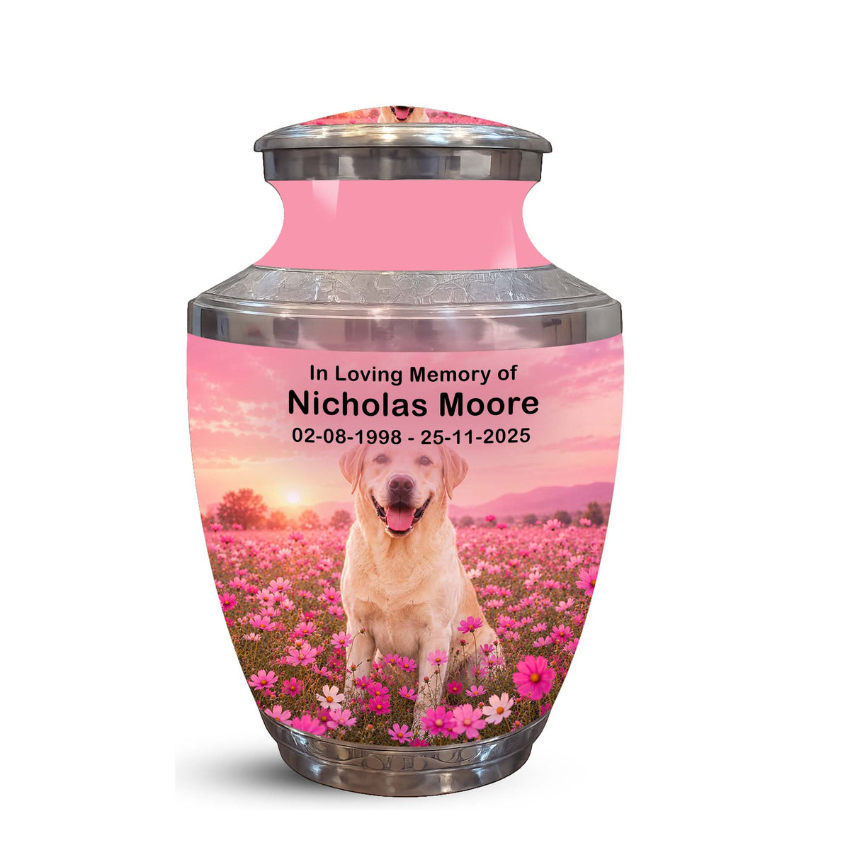 A memorial urn with a pink upper body and silver metallic rim and base, featuring a printed photo of a yellow Labrador retriever sitting in a pink flower field with sunset colors. Personalized text on the front reads: 'In Loving Memory of Nicholas Moore 02-08-1998 - 25-11-2025'.