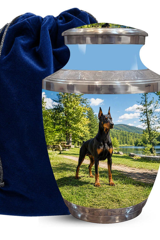 A memorial urn with a custom printed photo of a Doberman on the front, shown next to a dark blue velvet drawstring bag on a white background.