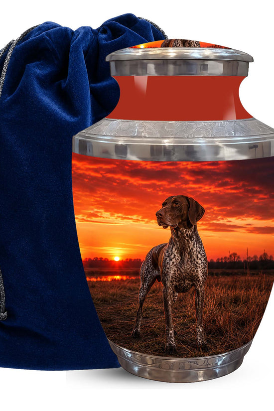 A memorial urn with a custom printed photo of a German Shorthaired Pointer dog at sunset, shown next to a dark blue velvet drawstring bag on a white background.