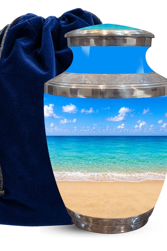 A glossy urn-shaped keepsake or cremation container with a tropical beach scene printed on the body, shown next to a dark blue velvet drawstring bag on a white background.