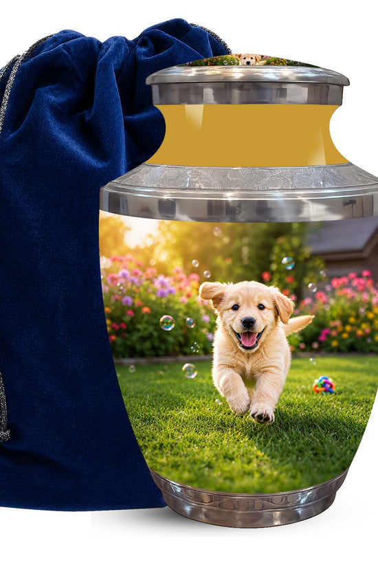 A pet memorial urn with a printed photo of a golden retriever puppy running on grass in a flower garden, shown next to a dark blue velvet drawstring bag on a white background.