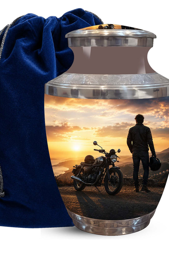 A ceramic cremation urn with a custom printed photo of a motorcycle rider at sunset, shown next to a dark blue velvet drawstring bag on a white background.