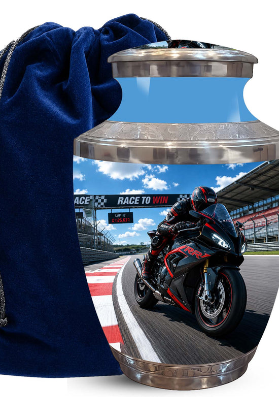 A glossy ceramic or glass memorial urn with a racing motorcycle graphic on the front, shown next to a dark blue velvet drawstring bag on a white background.