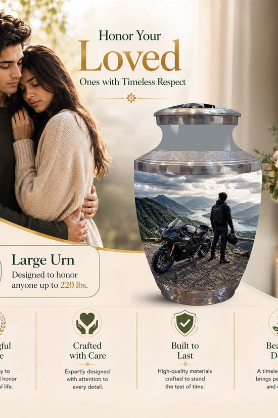 A large memorial urn displayed in a warm, styled setting with a couple in the background and text highlighting its features. The urn is clear glass with a printed scenic photo of a motorcycle rider on a mountain road, topped with a silver lid.