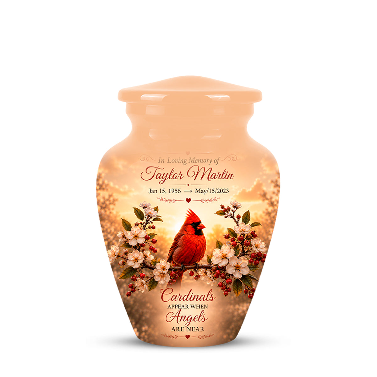 Personalized peach-colored ceramic cremation urn with a printed design of a red cardinal perched on white blossoms against a warm sunset sky. The front features customizable text reading 'In Loving Memory of Taylor Martin' and 'Cardinals appear when Angels are near'.